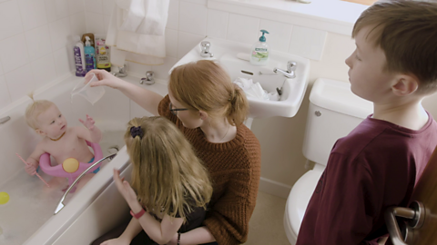 Toddler in bath as family talk and look on.