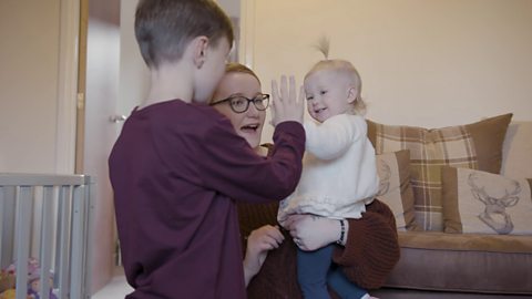 Mum holding toddler who is doing high five with brother.