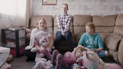 Family sat in lounge with lots of cuddly teddies. 