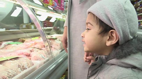 A little boy talking to the butcher at a supermarket.