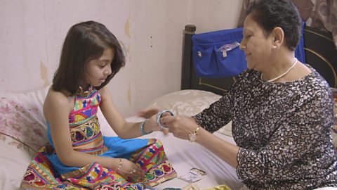 A little girl being shown how to wear traditional Gujurati dress.