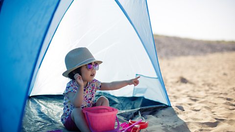 Child on the beach wearing a sun hat in the shade