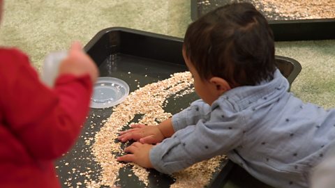 A baby using his hands to explore porridge in a tray.