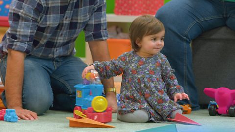 A young baby plays with a toy train on the floor.