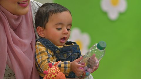 A small baby is fascinated by a homemade rattle, made with a plastic bottle.