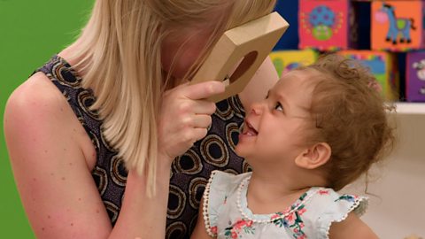 A parent looking through cardboard with a hole in it at her baby.