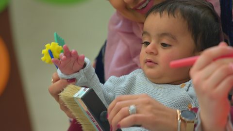 A baby plays with a large paintbrush, held by a parent