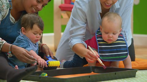 Two babies play with a tray of orange paint