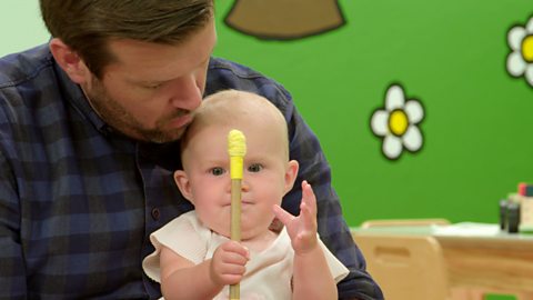 A baby plays with a stick that has yellow tape at the top of it.