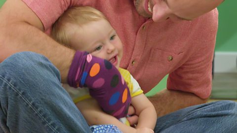 A baby laughing as a parent tickles them with a sock