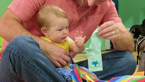 A parent holds a blue sock with a star on it in front of their baby