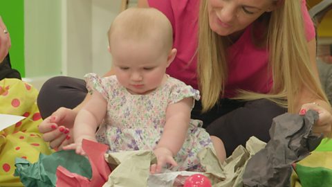 A parent sits with their baby among scraps of crumpled paper