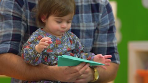 A parent coddles their baby while carrying a paper aeroplane