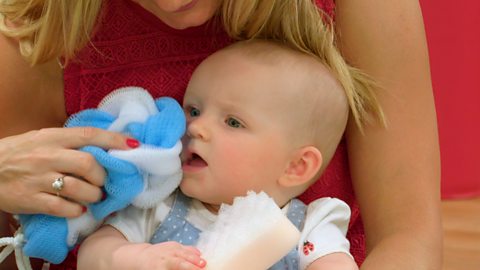 Mum pretends to wash her babies face with a blue and white sponge.