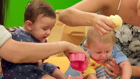 Two babies watch water falling from a sponge into a bucket or basin.