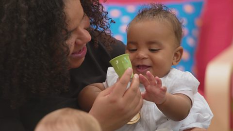 A parent giving a small plastic cup to a baby.