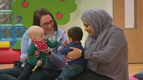 Two parents holding their babies, playing with toothbrushes