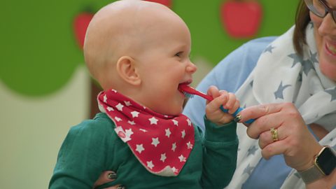 A parent is helping their baby pretend to brush their teeth