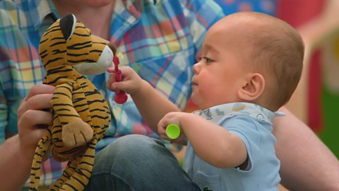 A baby pretends to brush the teeth of a plush tiger