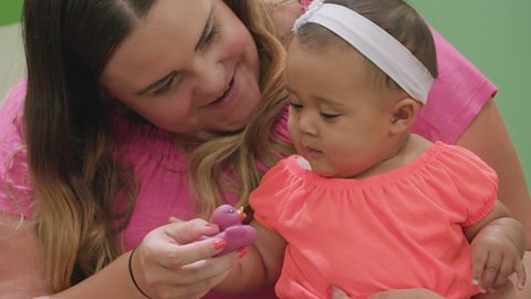 A parent offering a small pink rubber duck to their baby