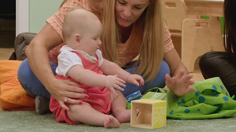 A parent playing with their baby and a hollow wooden box