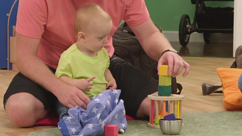 A parent stacks building blocks on top of each other while their baby watches