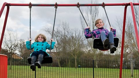 Two girls on swings in a play park