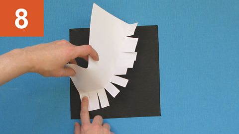 Step 8: Hands manipulate a sheet of paper into shape by glueing down its tabs