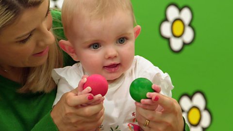 Baby sat on mum's knee holding two balls. 