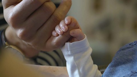 A very young baby gripping their mum's finger.