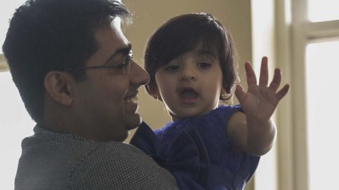 A little girl in her dad's arms holding up her hand.