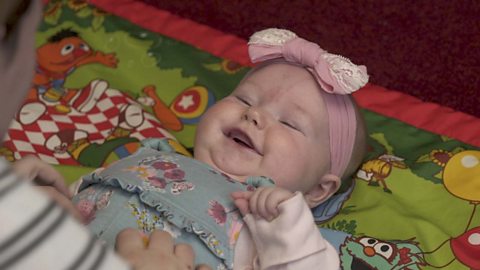 A baby girl looking up and laughing at her mum.