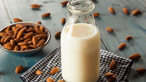 Bottle of dairy-free almond milk with almonds scattered behind it