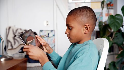 A boy is watching a documentary on a tablet for a secondary sources of information