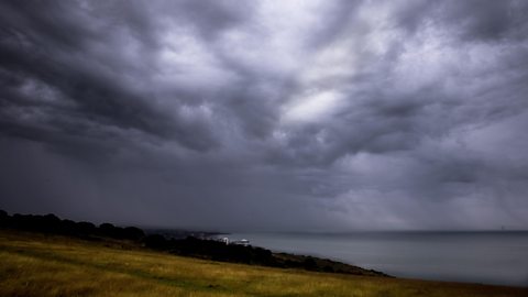 Low, threatening cumulonimbus clouds with falling rain hang over the sea.