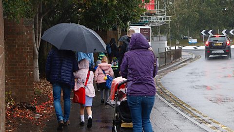 Families walking to school in the rain with umbrellas and rain jackets on