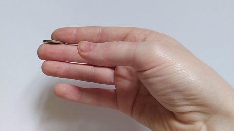 Close up of a hand holding a 20p piece between the index and middle finger.