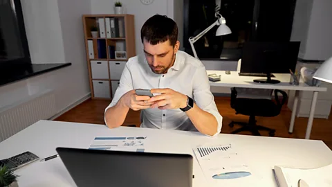 File image of a man looking at his phone in front of his laptop