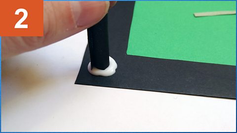 A hand presses a spacer into a blob of glue on a frame