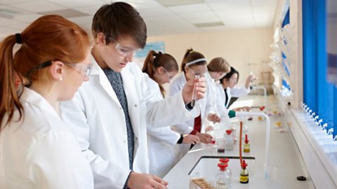 Six students wearing lab coats carrying out science experiments in pairs.