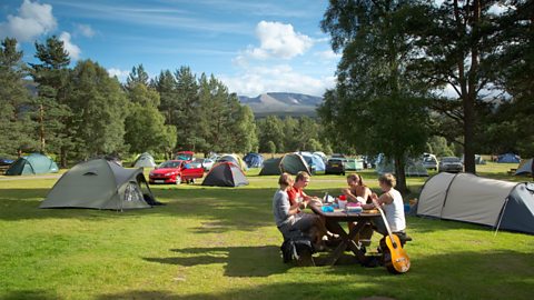 Group of friends enjoying a picnic at a picnic bench on a campsite