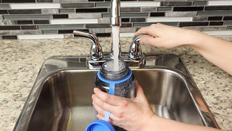 Hand filling up a reusable water bottle from the tap