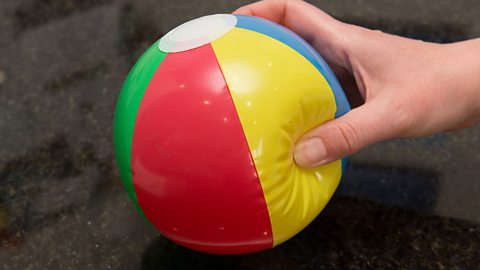 A hand sqeezing a small inflatable beach ball