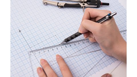 A hand holding a pencil plots points on a piece of graph paper