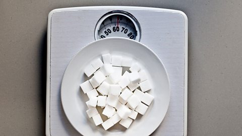 Sugar cubes on scales; the cubes are on a white plate.