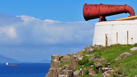 A foghorn perched on a cliff overlooking a ship at sea