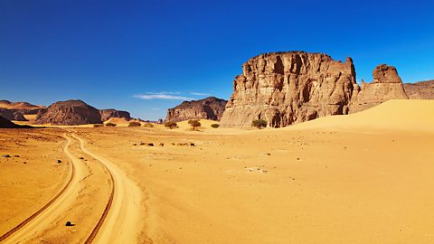 A dry desert area with sand and rocks, against a a blue sky.