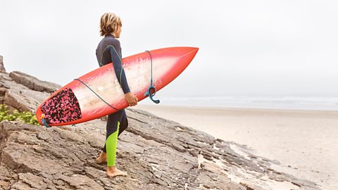 A boy holding a surfboard and looking out to sea