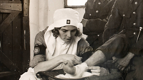 A nurse from the Voluntary Aid Detachment treats an injured soldier's leg during World War One.