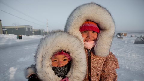 Two Inuit girls wear fur hooded jackets